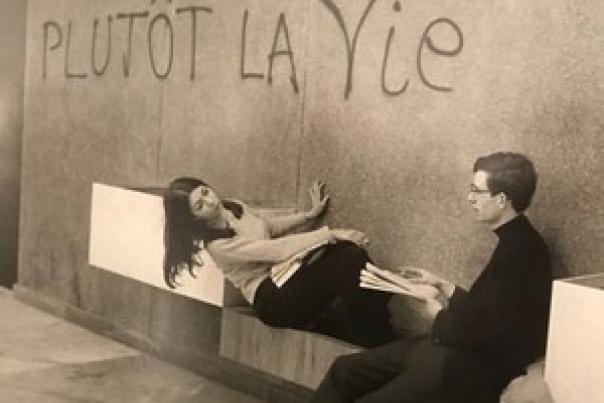 Deux personnes assises contre un mur où se trouve un graffiti "Plutôt la vie"