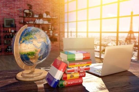 Un bureau sur lequels sont posés une map monde et une pile de dictionnaires dans différentes langues 