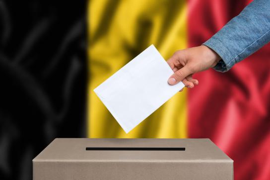 shutterstock_487377016-main qui glisse un billet dans une urne avec un drapeau belge en fond d'image